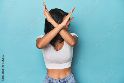 Filipina young woman on blue studio keeping two arms crossed, denial concept.