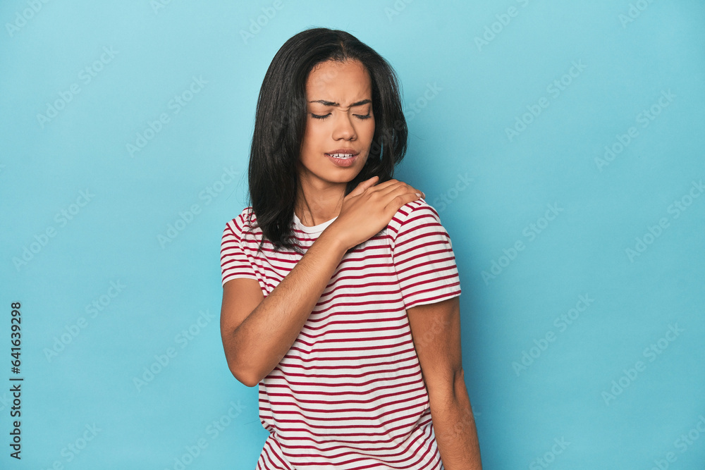 Filipina young woman on blue studio having a shoulder pain. Filipina young woman on blue studio having a shoulder pain.
