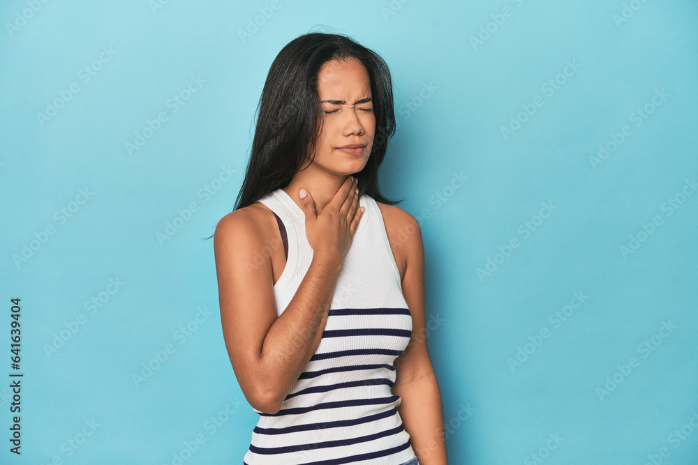 Filipina young woman on blue studio suffers pain in throat due a virus or infection. Filipina young woman on blue studio suffers pain in throat due a virus or infection.