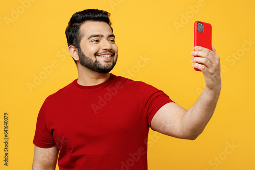 Photography Cheerful young happy Indian man he wears red t-shirt casual clothes doing selfie shot on mobile cell phone post photo on social network isolated on plain yellow orange background