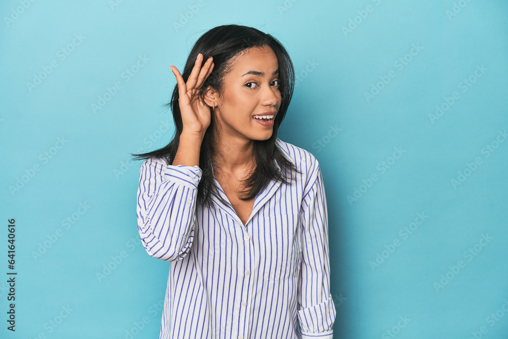 Filipina young woman on blue studio trying to listening a gossip. Filipina young woman on blue studio trying to listening a gossip.