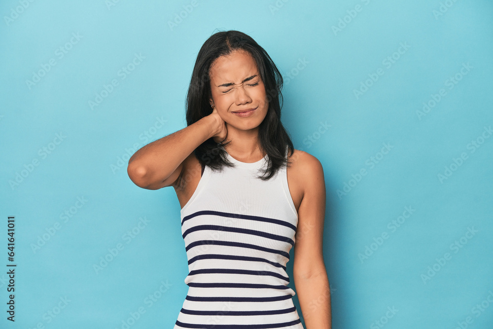 Filipina young woman on blue studio having a neck pain due to stress, massaging and touching it with hand.