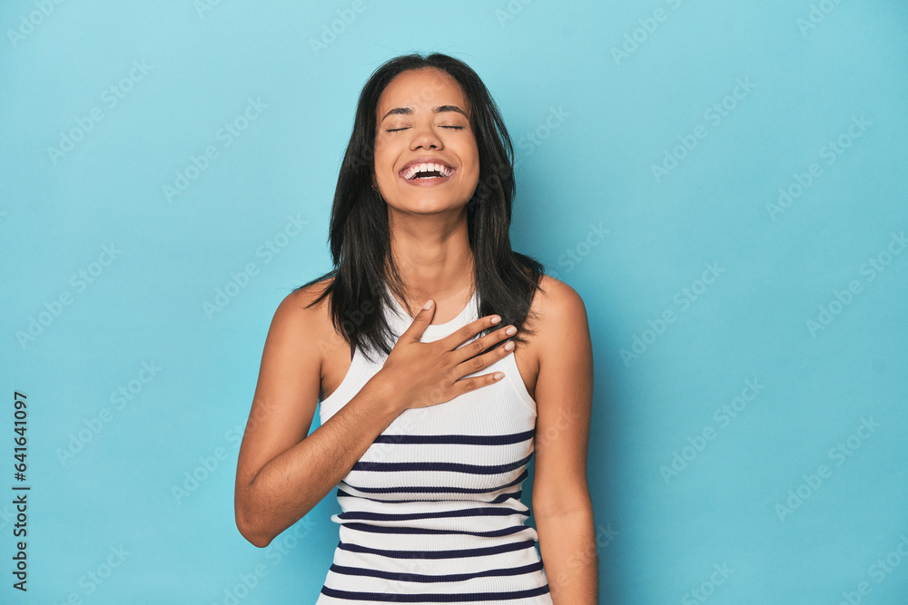 Filipina young woman on blue studio laughs out loudly keeping hand on chest. Filipina young woman on blue studio laughs out loudly keeping hand on chest.