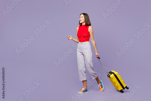Side view traveler woman wear red casual clothes hold suitcase walking going isolated on plain purple background. Tourist travel abroad in free spare time rest getaway Air flight trip journey concept. #641641059
