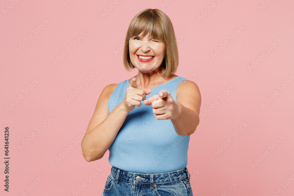 Elderly blonde woman 50s years old wears blue undershirt casual clothes point index finger camera on you motivating encourage isolated on plain pastel light pink background studio. Lifestyle concept. Elderly blonde woman 50s years old wears blue undershirt casual clothes point index finger camera on you motivating encourage isolated on plain pastel light pink background studio. Lifestyle concept.
