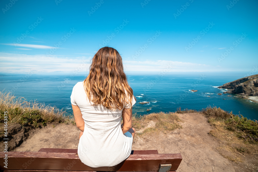 Seaside reflection: Woman seated on a coastal bench, contemplating the serene beauty of the paradisiacal beach. Seaside reflection: Woman seated on a coastal bench, contemplating the serene beauty of the paradisiacal beach.