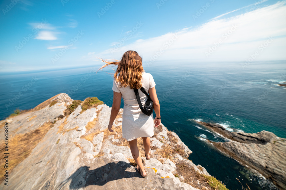Seeking serenity: Woman strolls to the rocky cliff's edge, embracing tranquility on a paradise beach. Seeking serenity: Woman strolls to the rocky cliff's edge, embracing tranquility on a paradise beach.