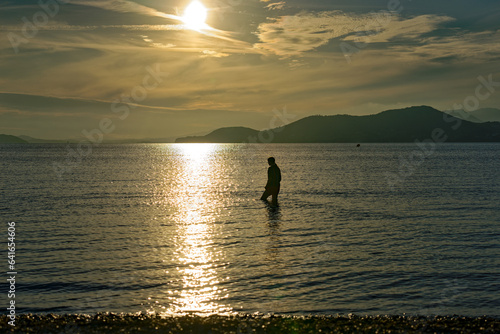 Beautiful sunset with colorful sky with silhouette of female teenager on a blue cloudy late spring evening at sandy beach of Giens Peninsula. Photo taken June 8th, 2023, Giens, Hyères, France.