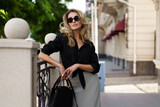 Outdoor portrait of beautiful elegant blond woman with perfect wavy hairs  holding luxury hand bag. Fashion acsessories, sunglasses.