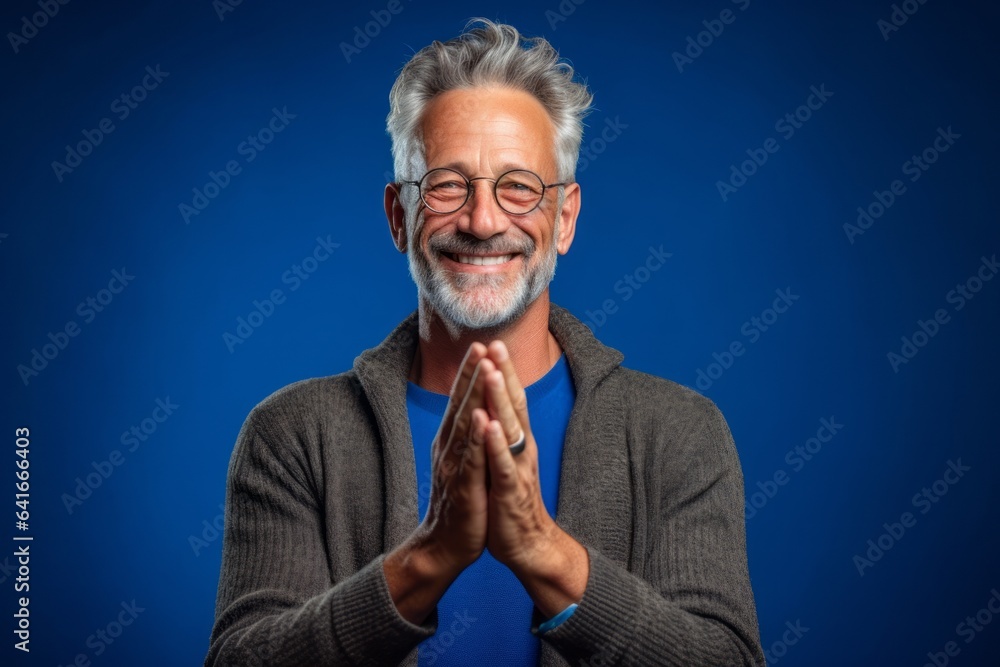 Lifestyle portrait photography of a satisfied mature man joining palms in a gesture of gratitude against a royal blue background. With generative AI technology Lifestyle portrait photography of a satisfied mature man joining palms in a gesture of gratitude against a royal blue background. With generative AI technology