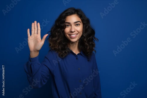 Medium shot portrait photography of a satisfied girl in her 20s making a no or stop gesture with the extended palm against a royal blue background. With generative AI technology