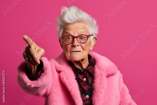 Medium shot portrait photography of a beautiful old woman pointing up against a hot pink background. With generative AI technology