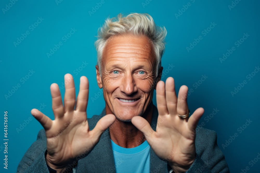 Close-up portrait photography of a beautiful mature man forming a circle with the fingers to say perfect against a teal blue background. With generative AI technology