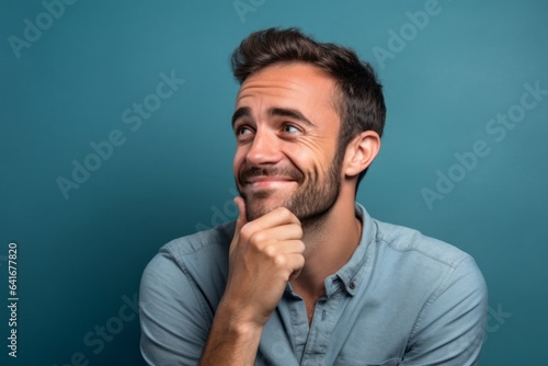 Close-up portrait photography of a joyful boy in his 30s putting the hand on the chin as if thinking against a soft blue background. With generative AI technology