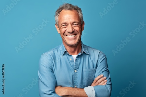 Medium shot portrait photography of a happy mature man crossing the arms against a soft blue background. With generative AI technology