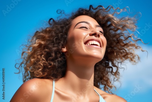 Close-up portrait photography of a grinning girl in her 20s laughing against a sky-blue background. With generative AI technology © Markus Schröder