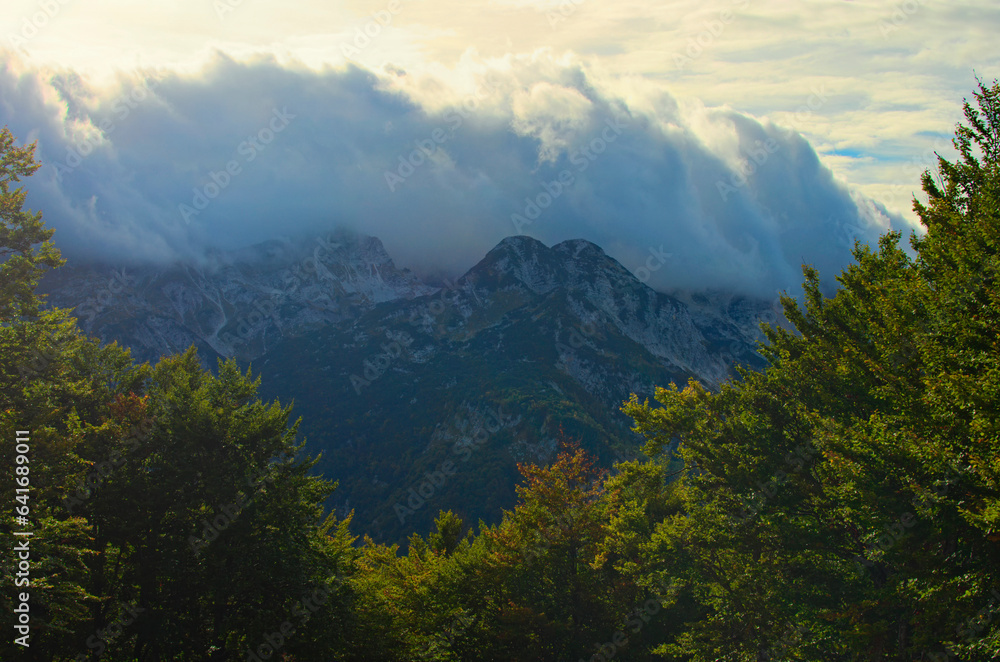 Picturesque nature landscape with heavy white clouds hang over beautiful mountain range. Landscape during the autumn season. Travel and tourism concept. Triglav National Park, Slovenia