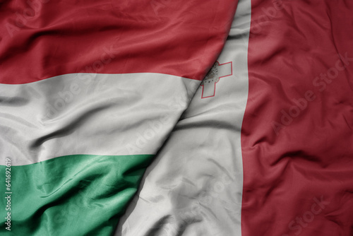 big waving national colorful flag of hungary and national flag of malta .