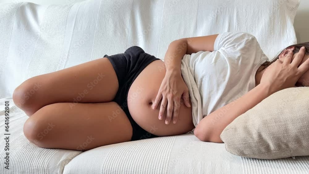 Pregnant woman lying on the sofa stroking her tummy. Concept of pregnancy and bad being Pregnant woman lying on the sofa stroking her tummy. Concept of pregnancy and bad being