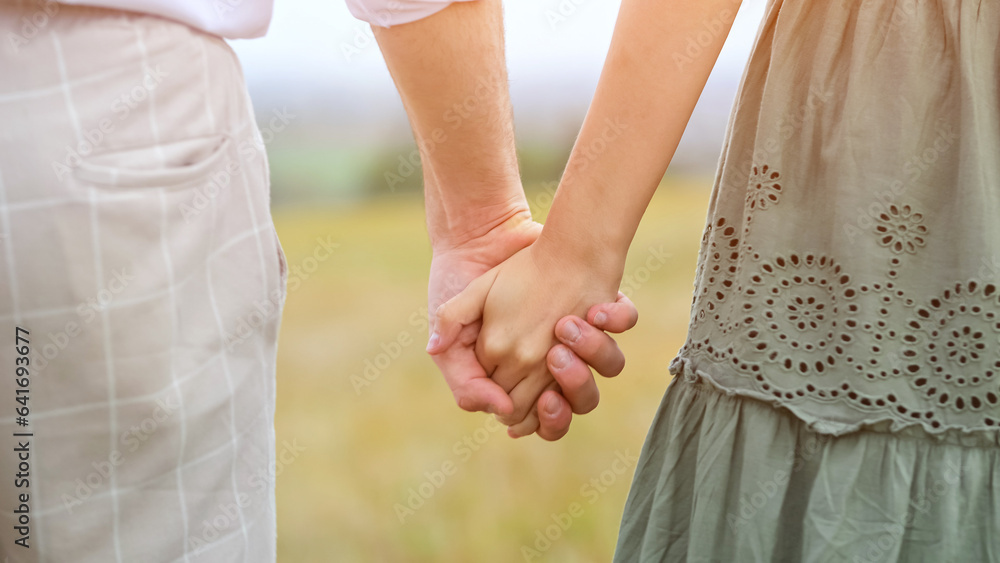 Couple of man and woman walk hand in hand across field on blurred background in warm season. Concept of love and interactions with partner, sunlight