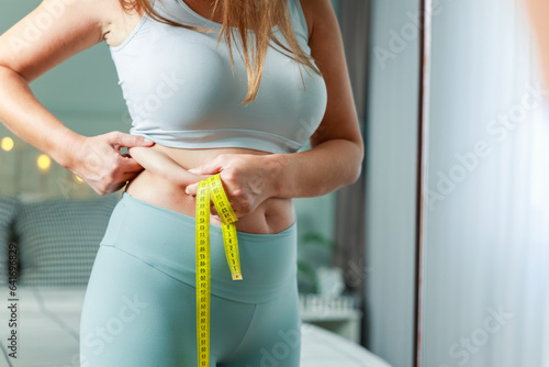 Fatty young woman hand holding excessive belly fat with measure tape, woman diet lifestyle photo