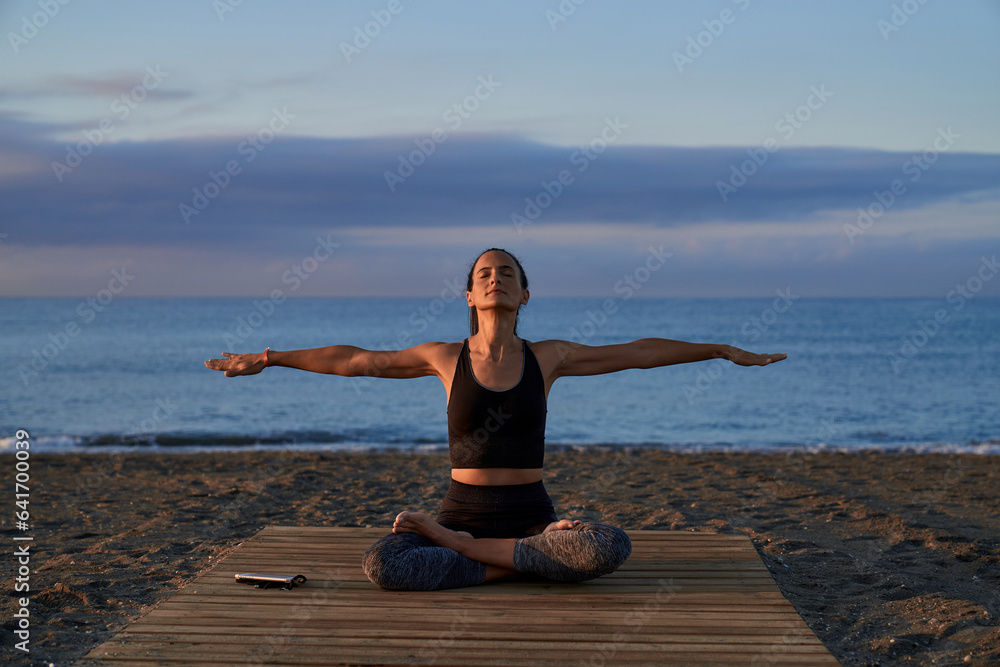 Hispanic woman in lotus pose with spread arms on shore