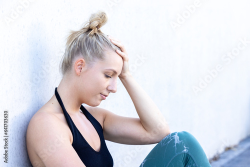 Fotografie In a candid portrayal of strength through adversity, a Caucasian blonde millennial sportswoman, donning her sports outfit, grapples with a sport injury