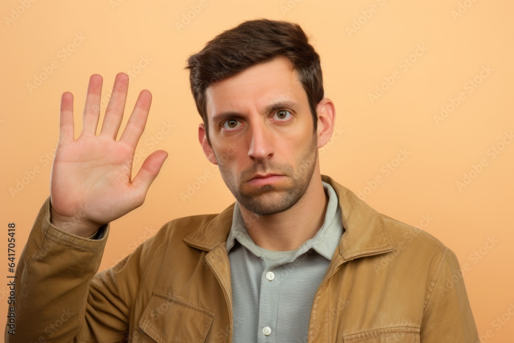 Naklejka premium Headshot portrait photography of a satisfied boy in his 30s making a no or stop gesture with the extended palm against a beige background. With generative AI technology