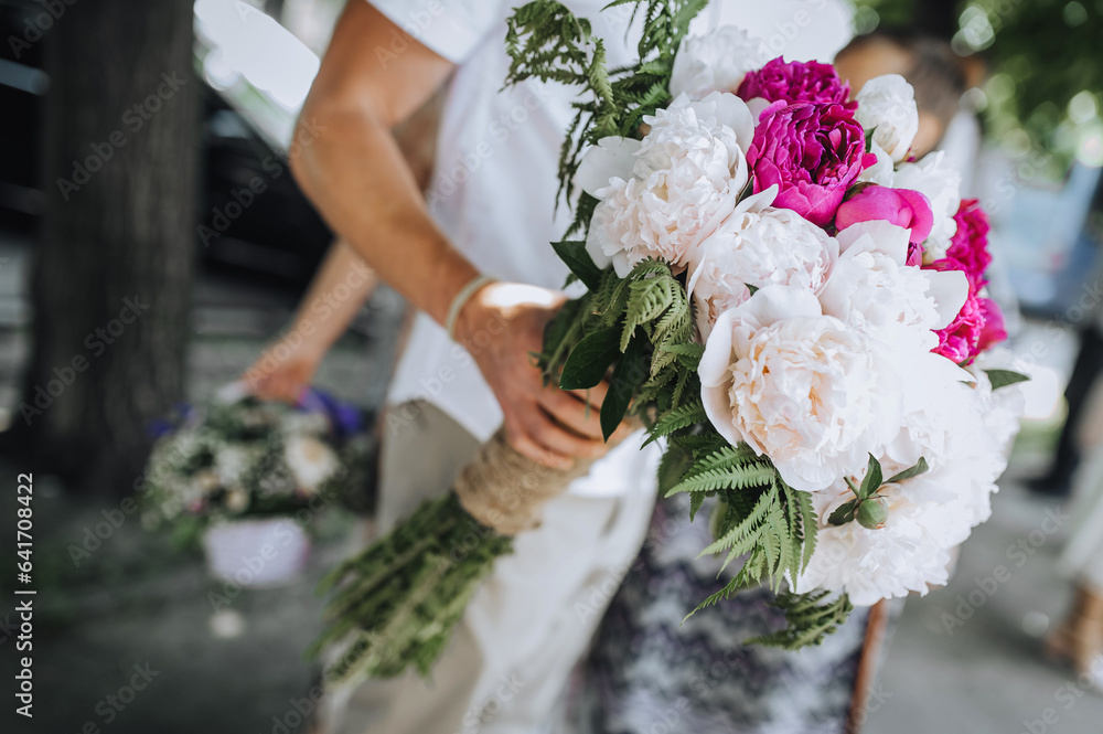 A man, a guest, holds a large beautiful bouquet of peonies of flowers at a birthday, wedding celebration. Close-up photography, portrait.