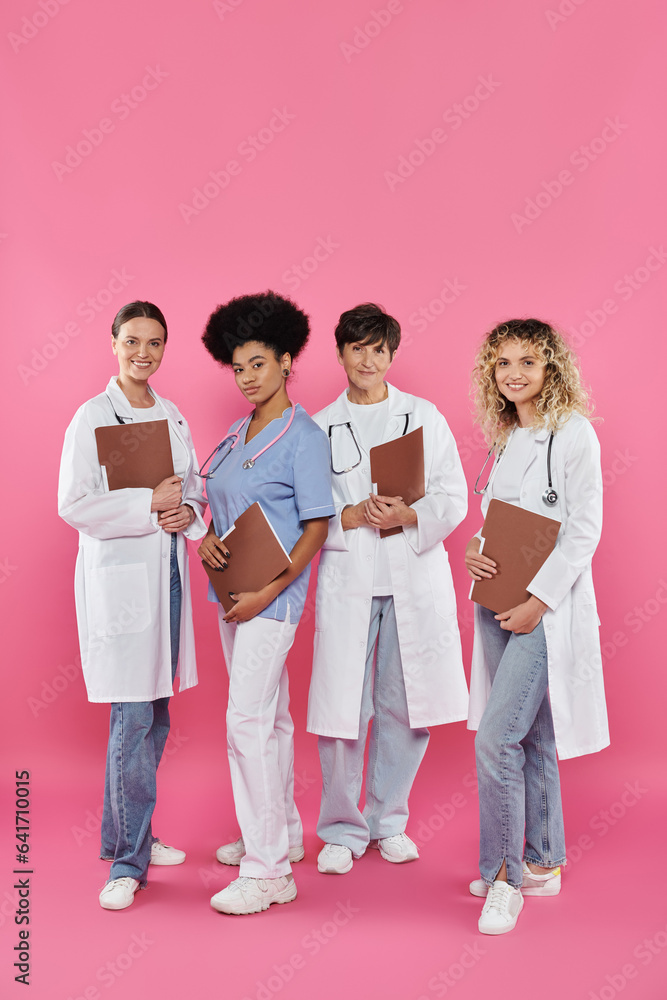 smiling multiethnic doctors with paper folders standing together on pink, breast cancer awareness smiling multiethnic doctors with paper folders standing together on pink, breast cancer awareness