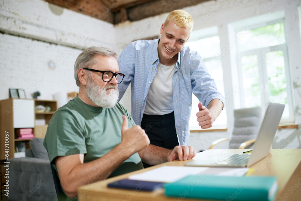 Cooperation of adults and youngsters. Young man helping senior businessman with technological issues on laptop. Concept of business, age diversity, education, modernity, innovations, assistance Cooperation of adults and youngsters. Young man helping senior businessman with technological issues on laptop. Concept of business, age diversity, education, modernity, innovations, assistance
