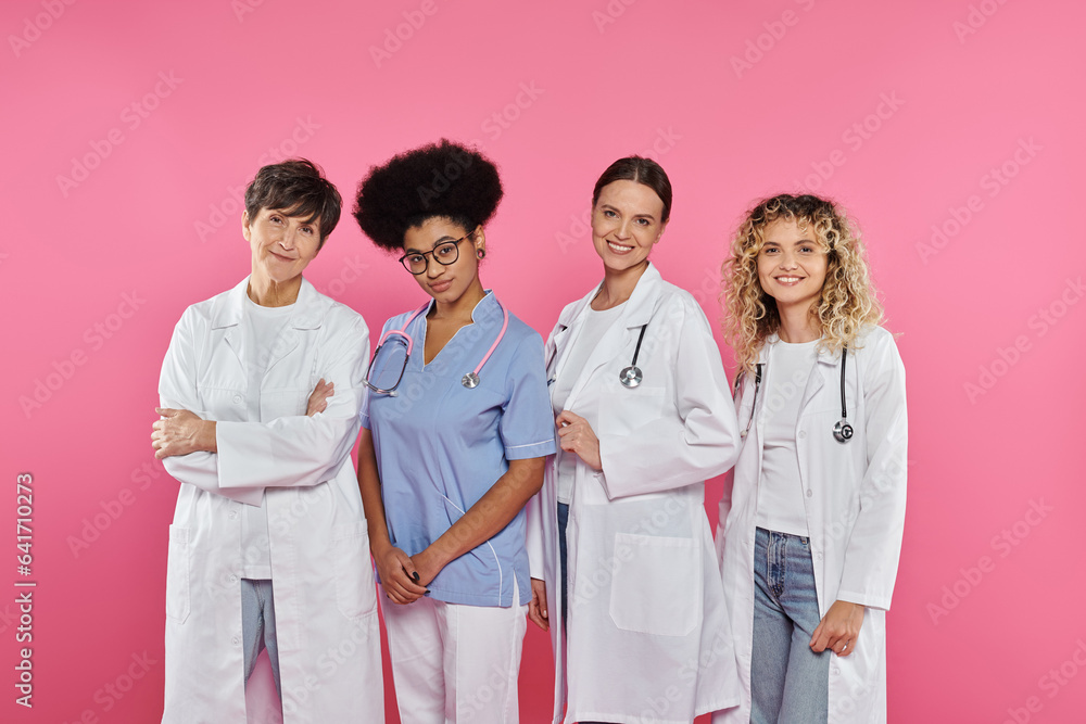 cheerful and multiethnic doctors smiling at camera isolated on pink, breast cancer concept cheerful and multiethnic doctors smiling at camera isolated on pink, breast cancer concept