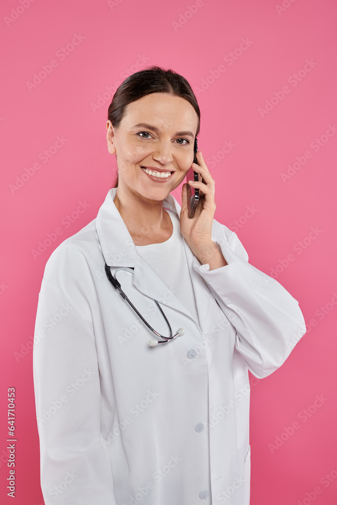 smiling female doctor talking on smartphone isolated on pink, breast cancer concept smiling female doctor talking on smartphone isolated on pink, breast cancer concept