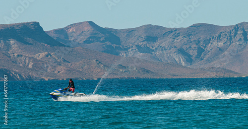 A guy on jet ski having fun in front of El Tecolote beach. In the background the isla Espiritu Santo on a sunny afternoon with blue sea and clear sky. La Paz Baja Mexico. photo
