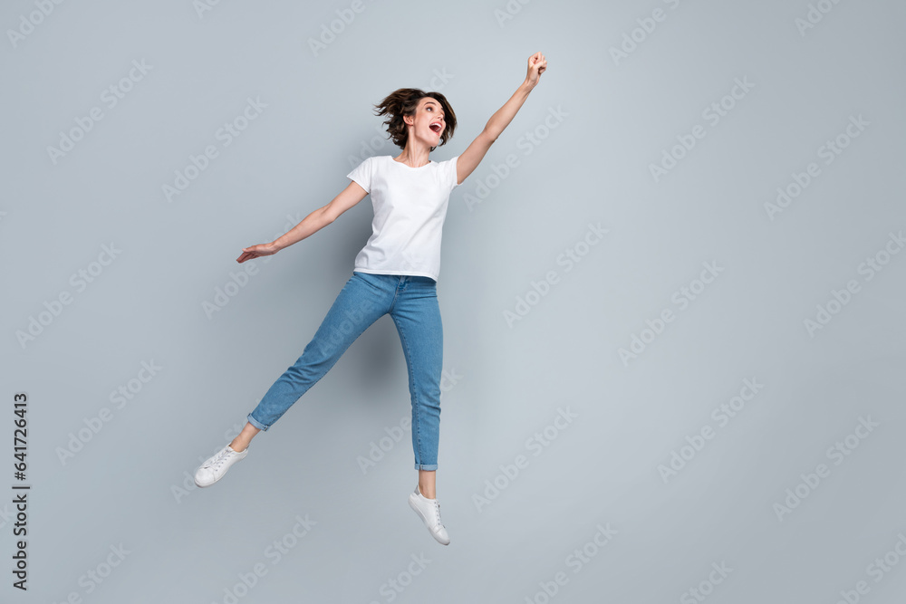 Full length photo of astonished woman wear stylish t-shirt flying like superhero look empty space isolated on gray color background