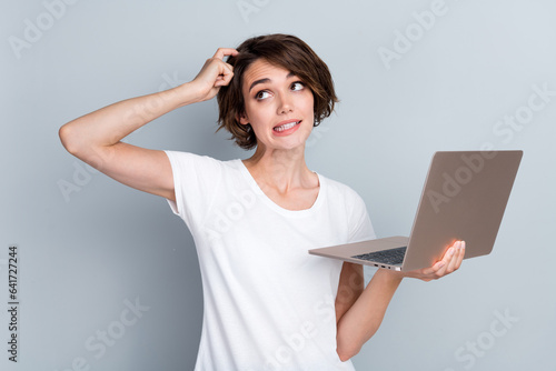 Portrait of puzzled woman wear stylish t-shirt hold laptop finger scratching head look empty space isolated on gray color background