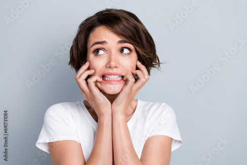 Photo of scared nervous lady wear white t-shirt biting fingers looking empty space isolated grey color background