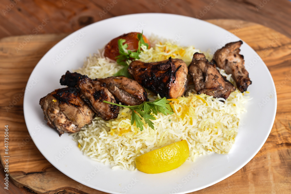 Joojeh Kebab rice or Jojeh Kabab with tomato and lime served in dish isolated on wooden table top view middle eastern lunch food Joojeh Kebab rice or Jojeh Kabab with tomato and lime served in dish isolated on wooden table top view middle eastern lunch food
