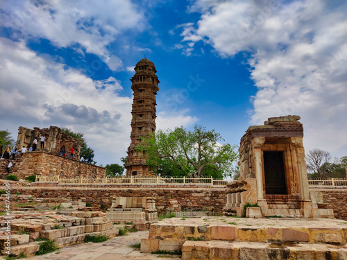 Picture of monument at Chittorgarh Fort with Vijay Stambha in background shot during daylight against blue sky and white clouds
 photo