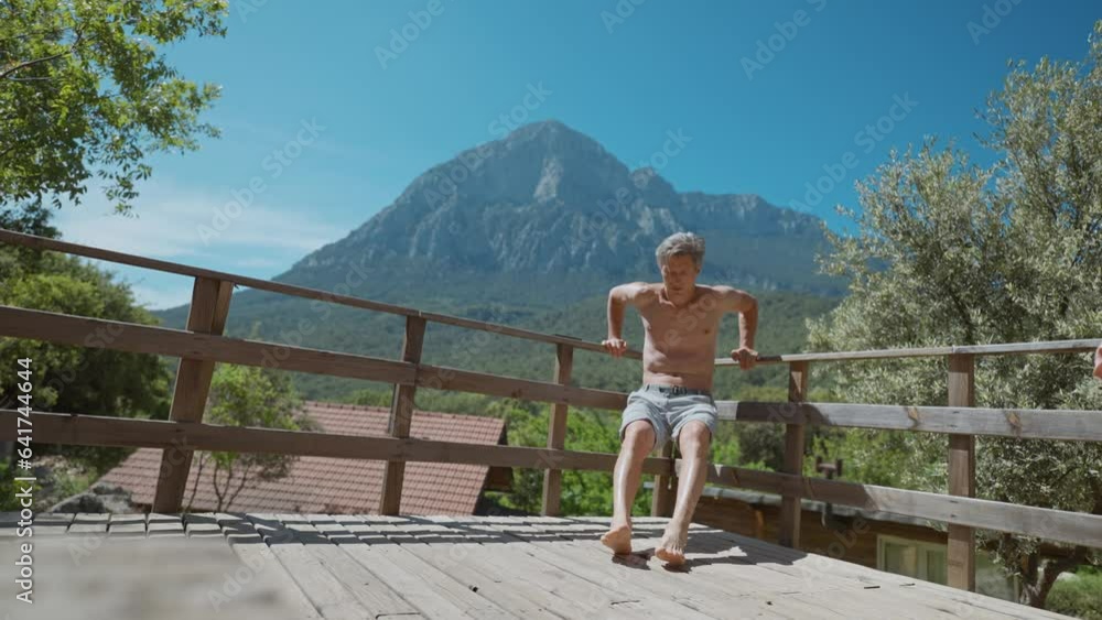 athletic aged sports man doing bodyweight push up and core exercises outdoors on wooden terrace outdoors. sport exercise with beautiful mountains background. active lifestyle. using mobile app athletic aged sports man doing bodyweight push up and core exercises outdoors on wooden terrace outdoors. sport exercise with beautiful mountains background. active lifestyle. using mobile app