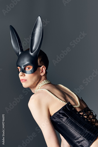 queer person in black corset and bdsm bunny mask posing on grey, corset lacing, edgy fashion