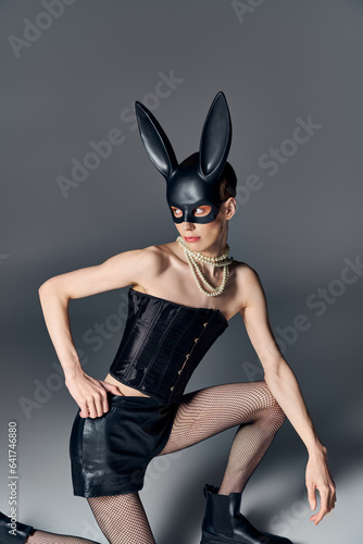 bold style, provocative person in corset posing in bdsm bunny mask on grey, queer fashion, look away