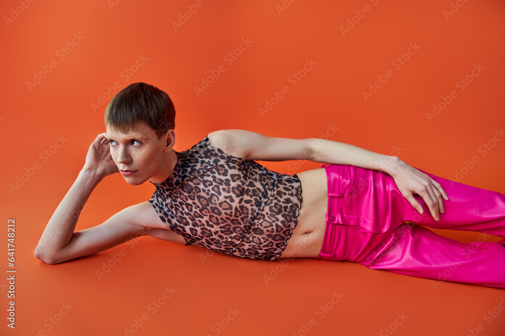 queer person in leopard print top and pink pants lying on orange backdrop, style and fashion queer person in leopard print top and pink pants lying on orange backdrop, style and fashion