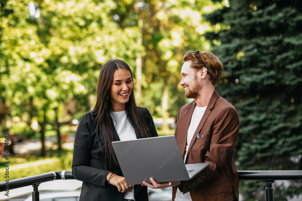 A handsome red-haired man and a brunette in business suits on a summer terrace. Senior entrepreneurs at a business meeting in an outdoor restaurant are discussing a project on a laptop. A handsome red-haired man and a brunette in business suits on a summer terrace. Senior entrepreneurs at a business meeting in an outdoor restaurant are discussing a project on a laptop.