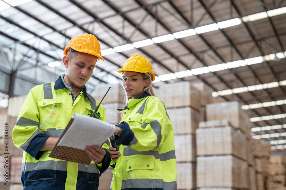 Man and woman workers in uniform with helmet safety holding clipboard discussing and checking wood plank material in pallet factory warehouse. Man and woman workers in uniform with helmet safety holding clipboard discussing and checking wood plank material in pallet factory warehouse.