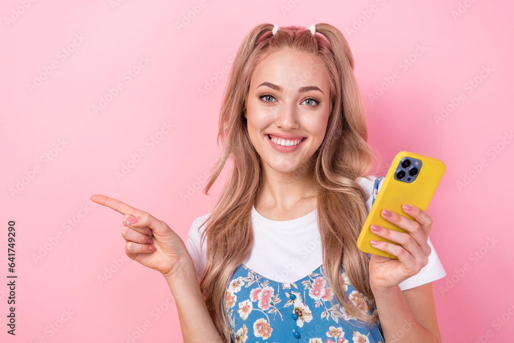 Photo portrait of lovely young lady pointing empty space telephone wear trendy flower print garment isolated on pink color background Photo portrait of lovely young lady pointing empty space telephone wear trendy flower print garment isolated on pink color background