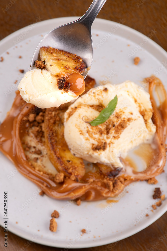 spoon showing tasting banoffee dessert with banana dulce de leche vanilla ice cream and ground biscuit top view