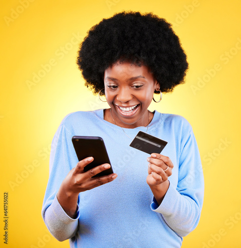 Happy black woman, phone and credit card in online shopping against a yellow studio background. Excited African female person with afro smile on mobile smartphone app in ecommerce, payment or banking