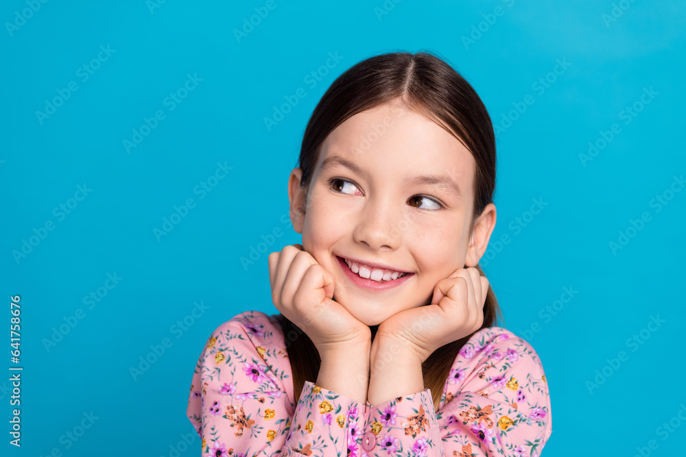 Photo portrait of pretty schoolkid look empty space touch cheeks dressed stylish pink flower print outfit isolated on blue color background Photo portrait of pretty schoolkid look empty space touch cheeks dressed stylish pink flower print outfit isolated on blue color background