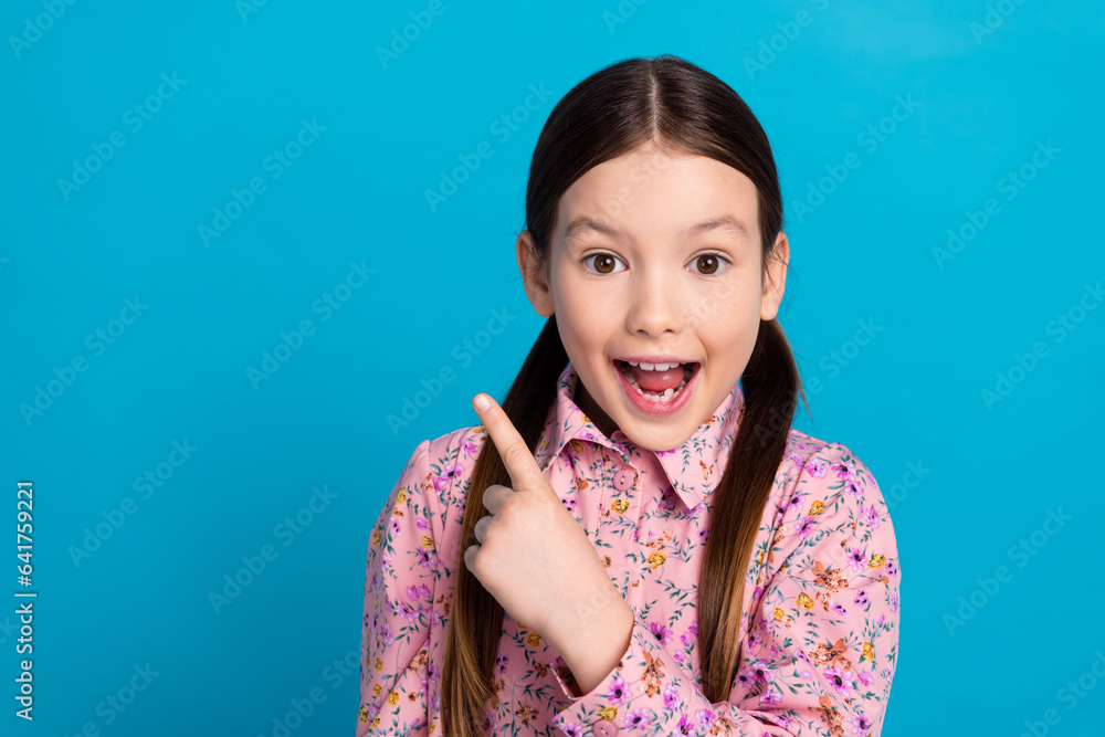 Photo portrait of lovely schoolkid girl pointing empty space dressed stylish pink flower print garment isolated on blue color background Photo portrait of lovely schoolkid girl pointing empty space dressed stylish pink flower print garment isolated on blue color background